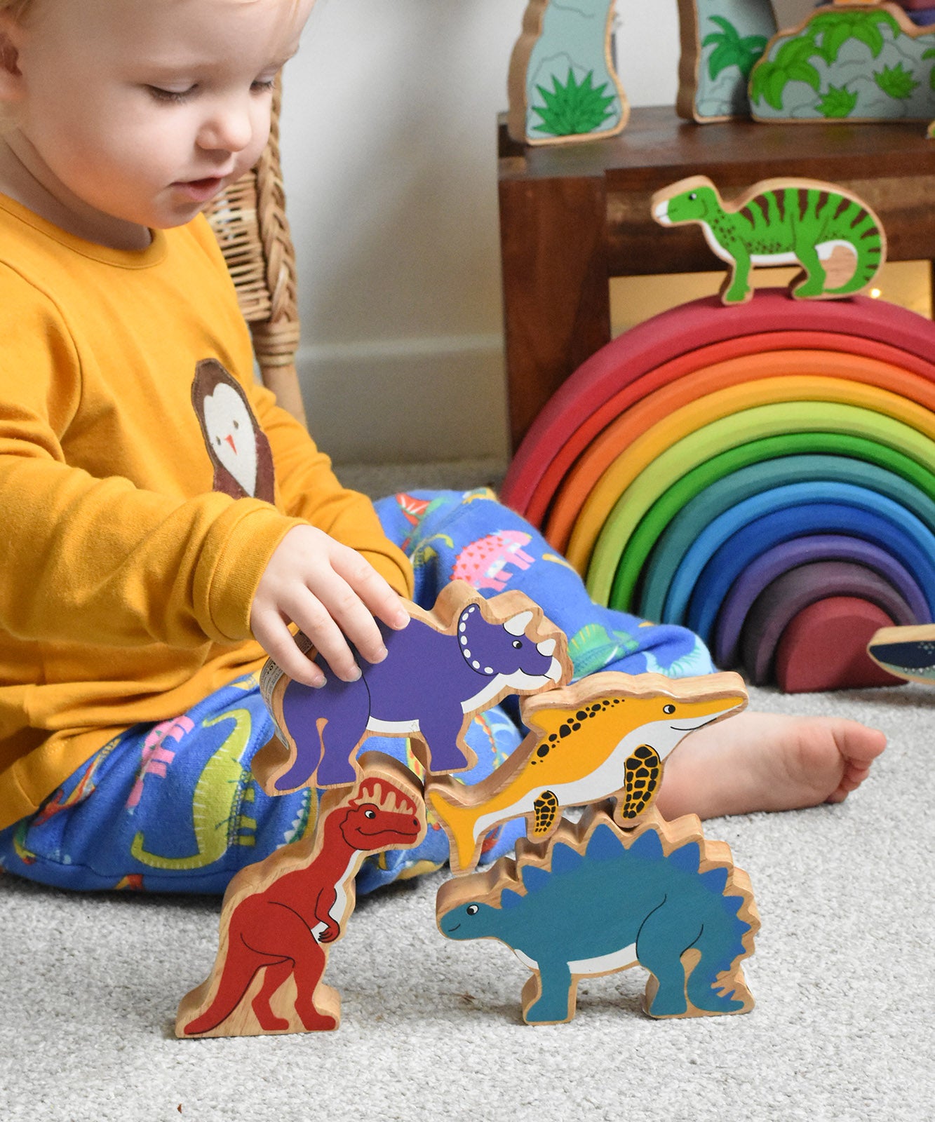 A child playing with Lanka Kade wooden toy animal figures. The child has his hand on a purple dinosaur figure. These wooden toy figures are part of a huge range of Lanka Kade fair trade, wooden toys available here at Babipur.