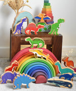 A large collection of Lanka Kade wooden toy dinosaur figures placed on a small wooden table and a Grimm's rainbow. These wooden toy figures are part of a huge range of Lanka Kade fair trade, wooden toys available here at Babipur.