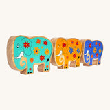 A side angle of the green, yellow and blue wooden Lanka Kade elephants on a cream background.