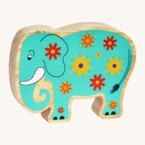 A green wooden Lanka Kade elephant with yellow and red flowers on a cream background.