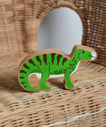 A Lanka Kade green iguanodon wooden toy figure placed on a child's wicker chair. These wooden toy figures are part of a huge range of Lanka Kade fair trade, wooden toys available here at Babipur.