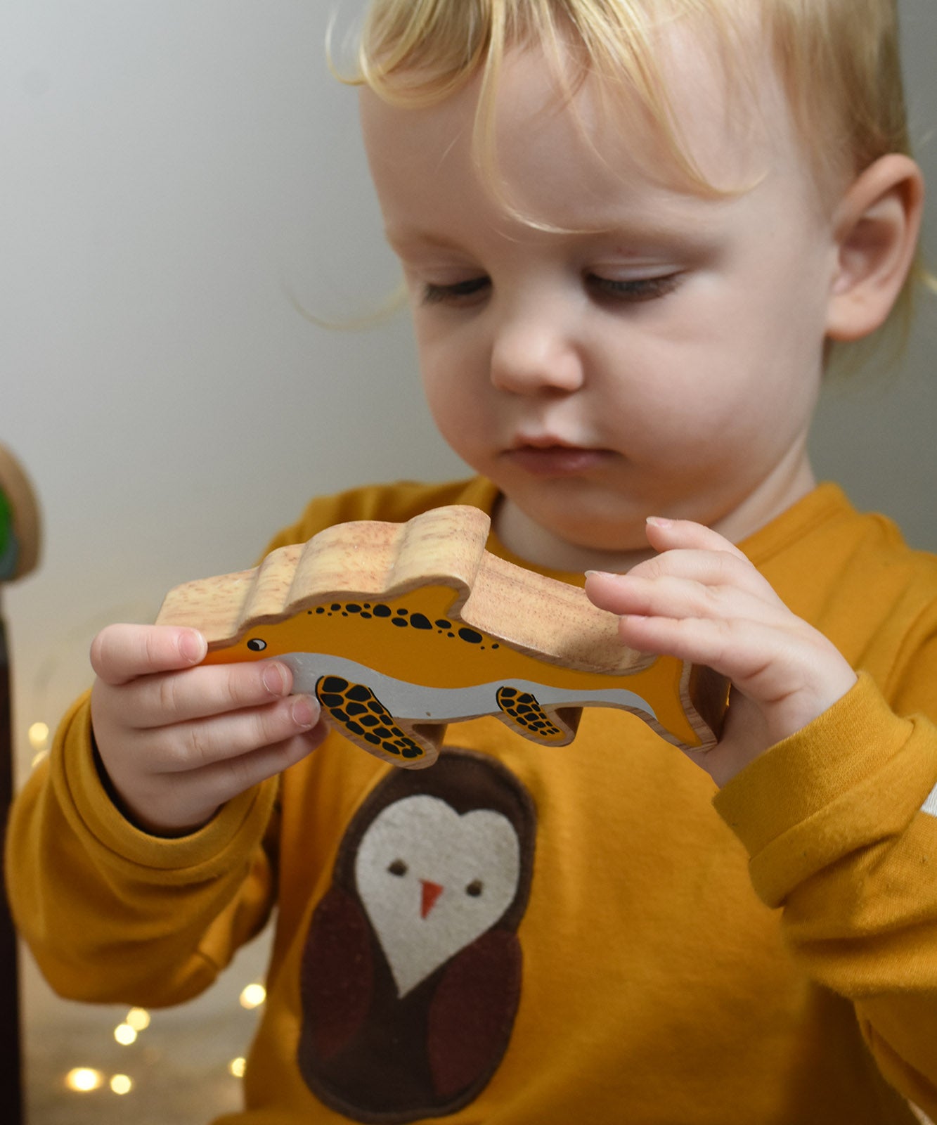 A child holding and inspecting a yellow Lanka Kade icthyosaur wooden toy figure. These wooden toy figures are part of a huge range of Lanka Kade fair trade, wooden toys available here at Babipur.