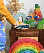 A child playing with Lanka Kade wooden toy dinosaur figures. The child is holding the ichthyosaur in their hand. These wooden toy figures are part of a huge range of Lanka Kade fair trade, wooden toys available here at Babipur.