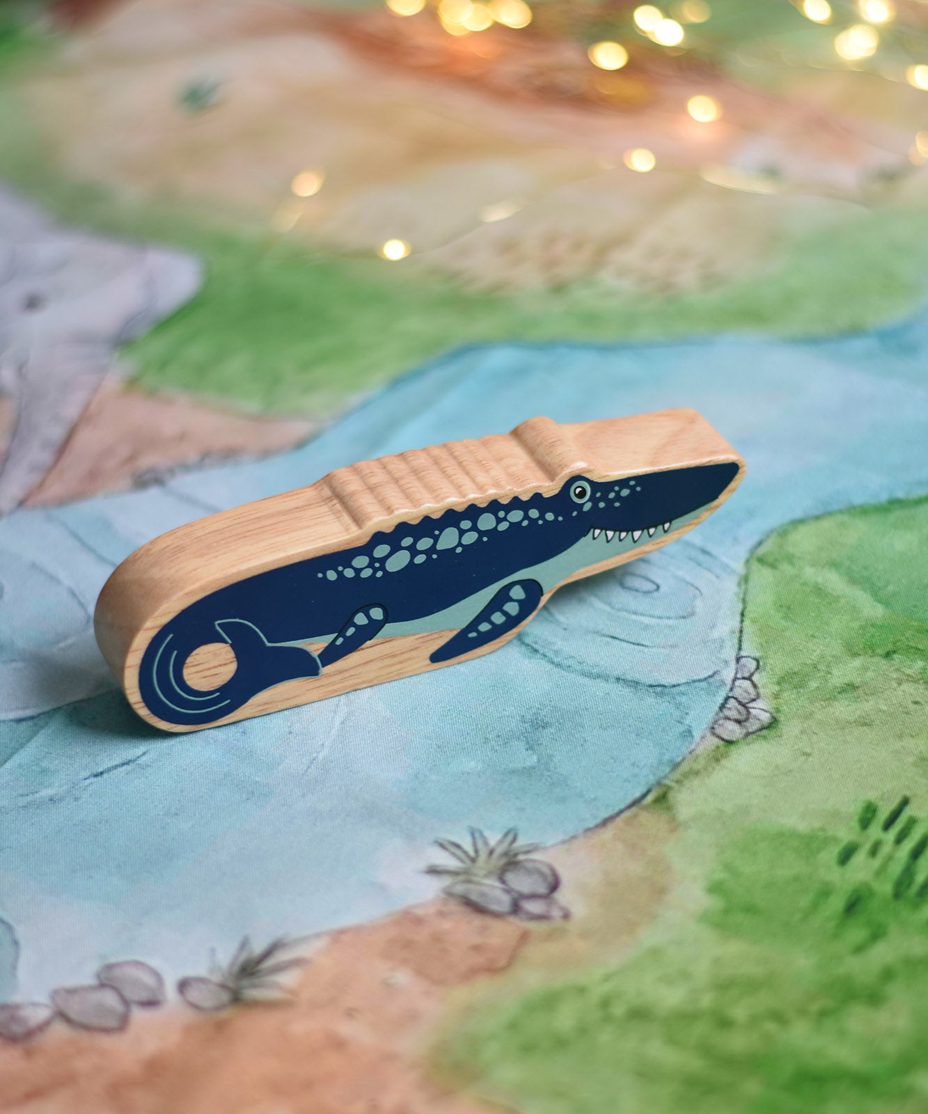 A Lanka Kade mosasurus wooden toy figure placed on a Wonderie plains of Africa play cloth. These wooden toy figures are part of a huge range of Lanka Kade fair trade, wooden toys available here at Babipur.