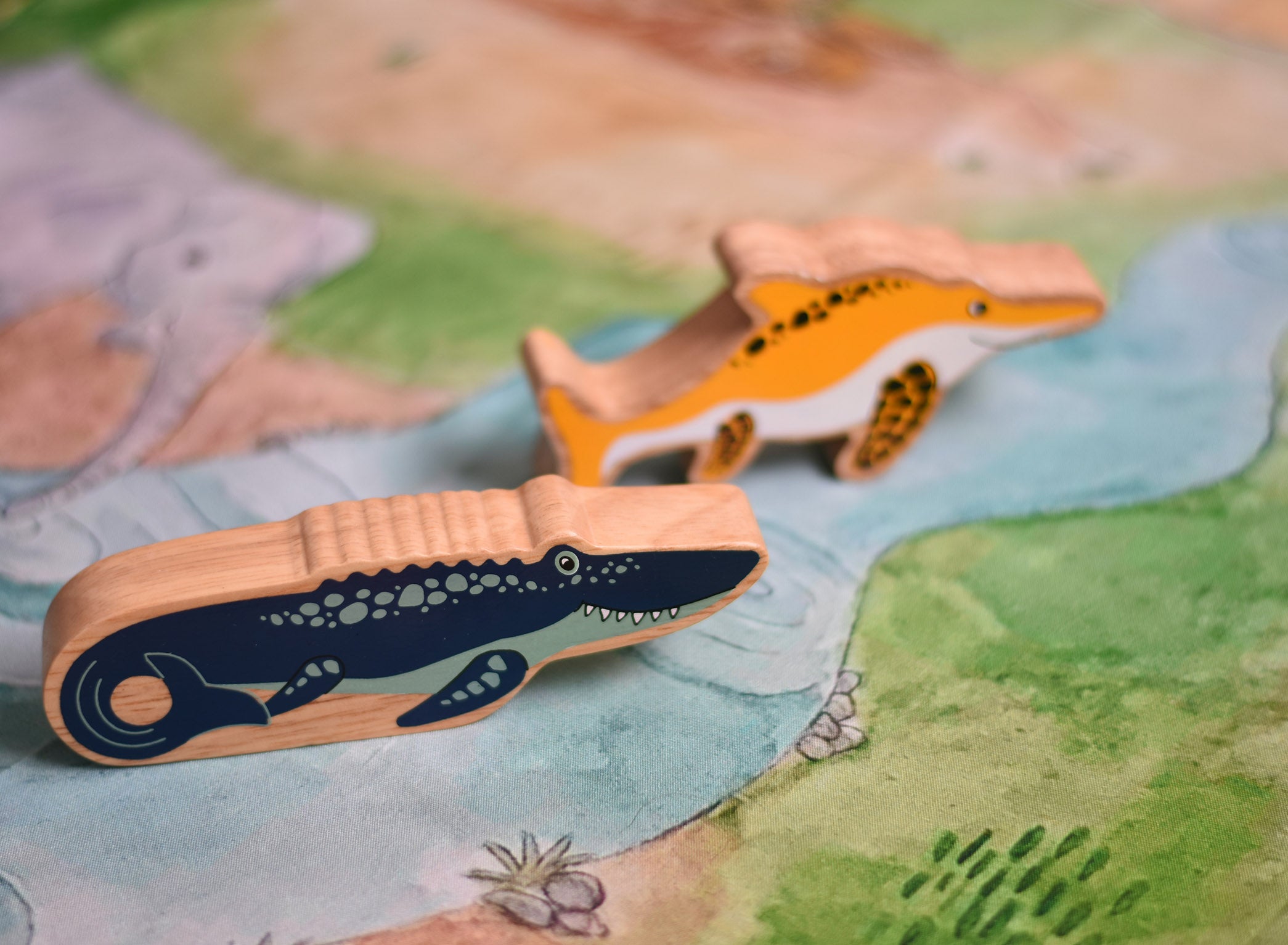 A Lanka Kade mosasurus wooden toy figure placed on a Wonderie plains of Africa play cloth. These wooden toy figures are part of a huge range of Lanka Kade fair trade, wooden toys available here at Babipur.