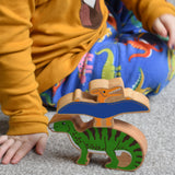 A close up of child playing with Lanka Kade wooden toy dinosaur figures. The child is pointing at the Lanka Kade pteranodon figure that has been stacked n top of a iguanodon dinosaur figure. These wooden toy figures are part of a huge range of Lanka Kade fair trade, wooden toys available here at Babipur.