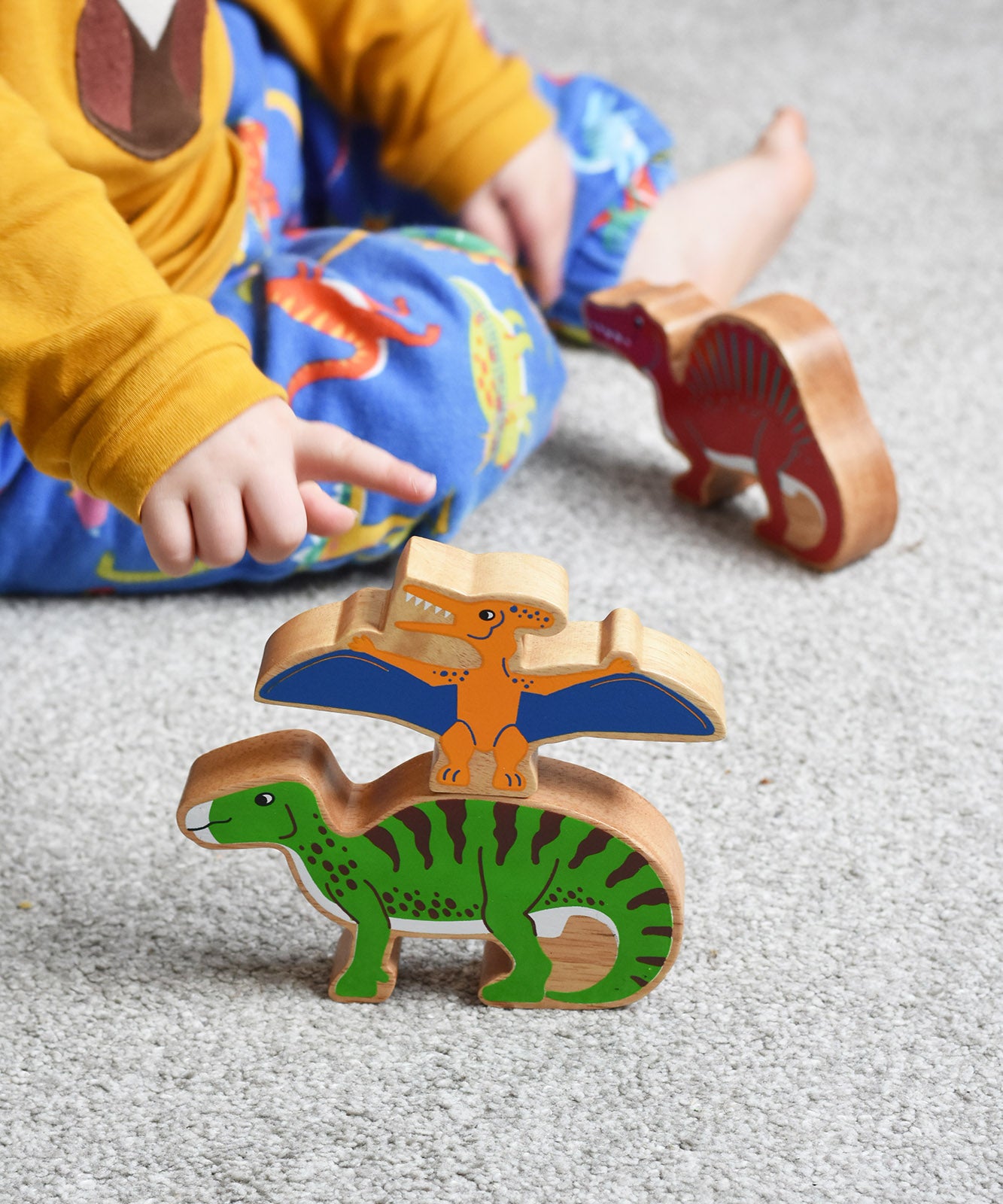 A child playing with Lanka Kade wooden toy dinosaur figures. The child is pointing at the Lanka Kade pteranodon figure. These wooden toy figures are part of a huge range of Lanka Kade fair trade, wooden toys available here at Babipur.