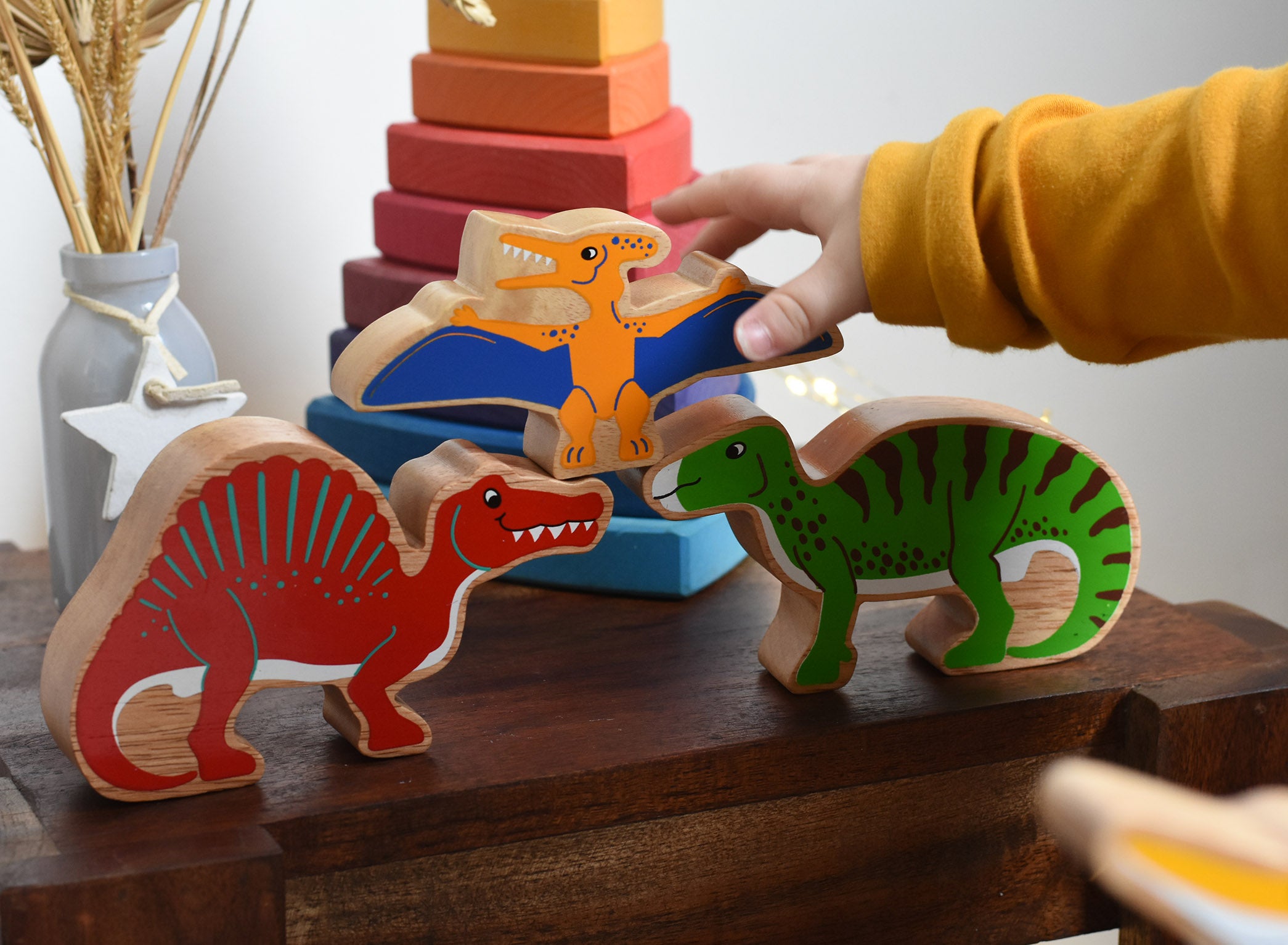 A child playing with Lanka Kade wooden toy dinosaur figures. The child is reaching for the Lanka Kade pteranodon figure. These wooden toy figures are part of a huge range of Lanka Kade fair trade, wooden toys available here at Babipur.