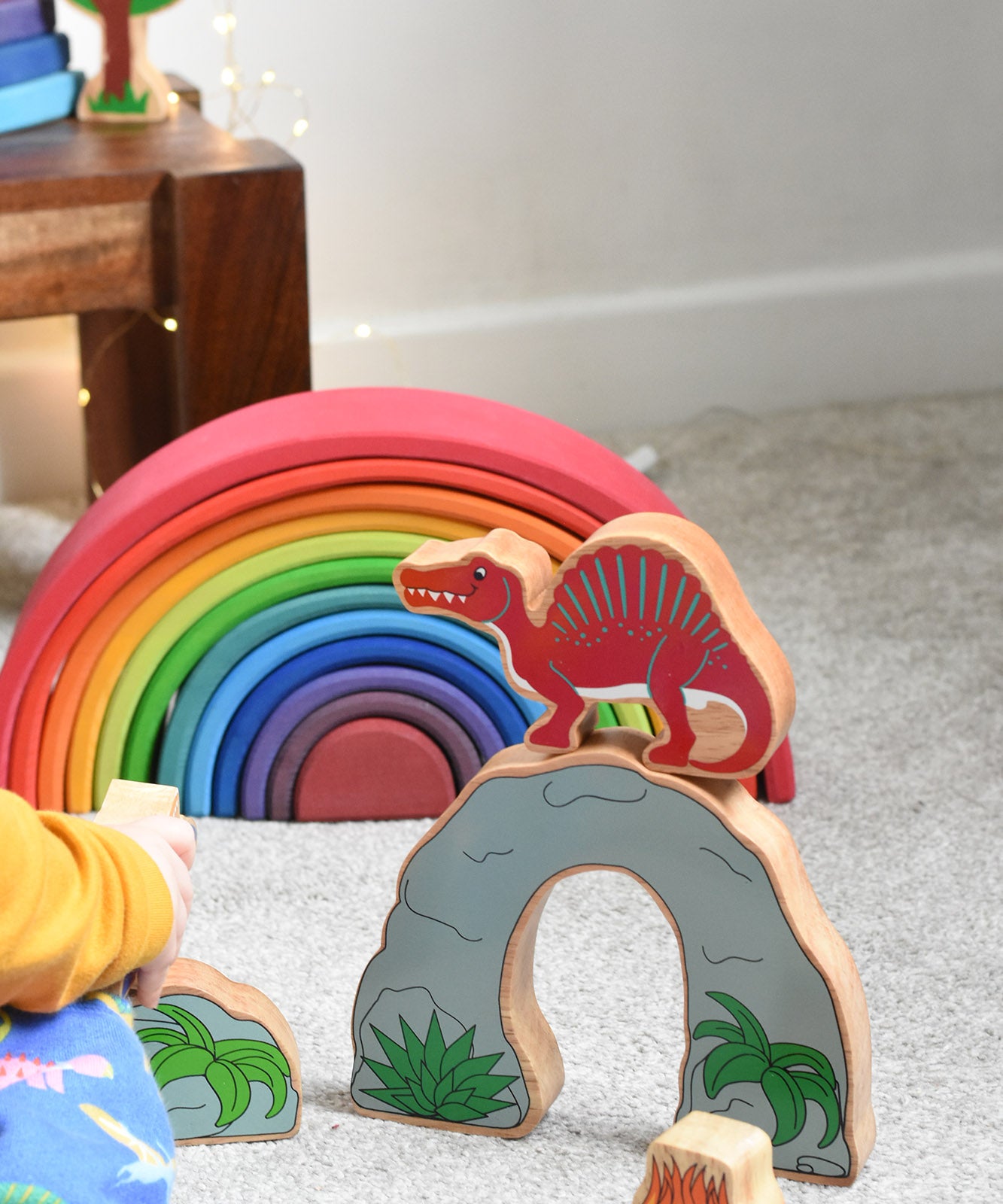 The Lanka Kade Wooden red Spinosaurus Dinosaur figure placed on a Lanka Kade cave from the prehistoric playset. These wooden toy figures are part of a huge range of Lanka Kade fair trade, wooden toys available here at Babipur.