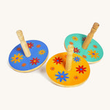 A blue, yellow and green wooden Lanka Kade spinning top next to each other on a cream background.