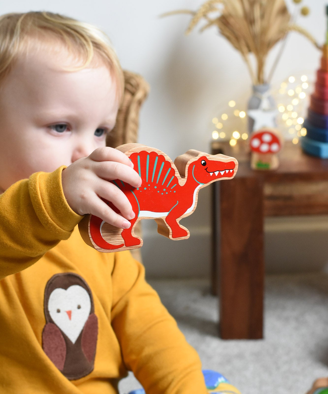 A child holding the Lanka Kade Wooden Spinosaurus Dinosaur in their hand. These wooden toy figures are part of a huge range of Lanka Kade fair trade, wooden toys available here at Babipur.