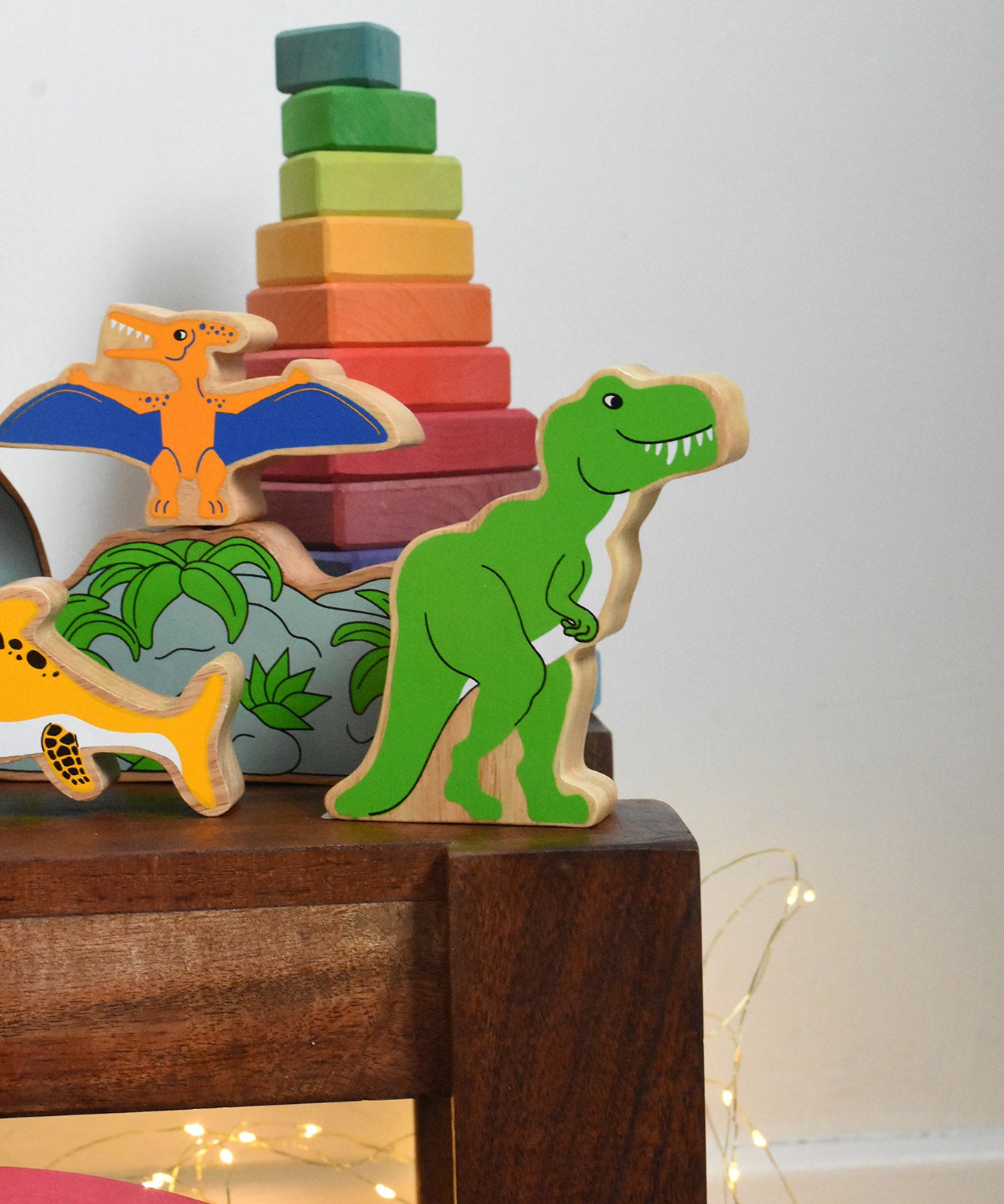 A Lanka Kade T Rex Dinosaur wooden toy figure placed on a small wooden table. These wooden toy figures are part of a huge range of Lanka Kade fair trade, wooden toys available here at Babipur.