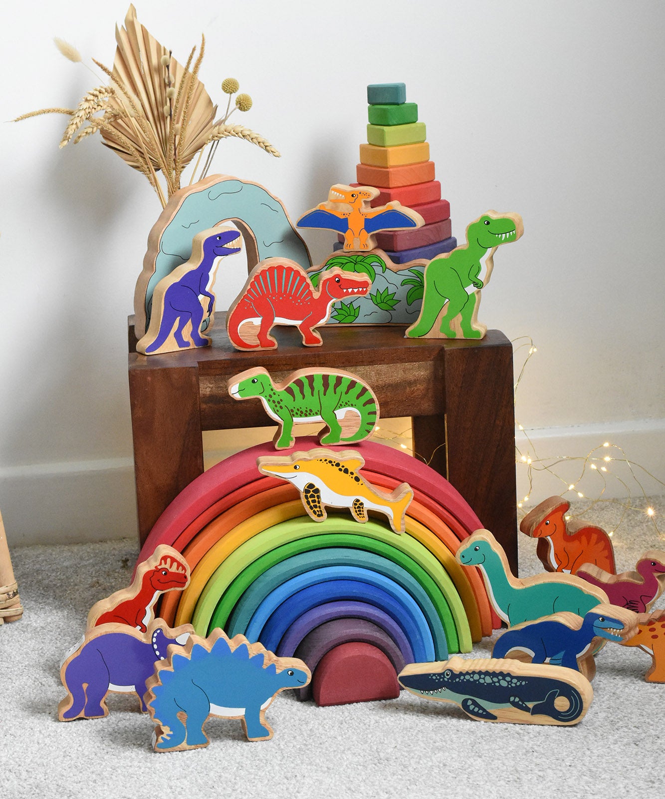 A collection of wooden dinosaur figures from Lanka Kade place on a small wooden table and Grimm's rainbow. These wooden toy figures are part of a huge range of Lanka Kade fair trade, wooden toys available here at Babipur.