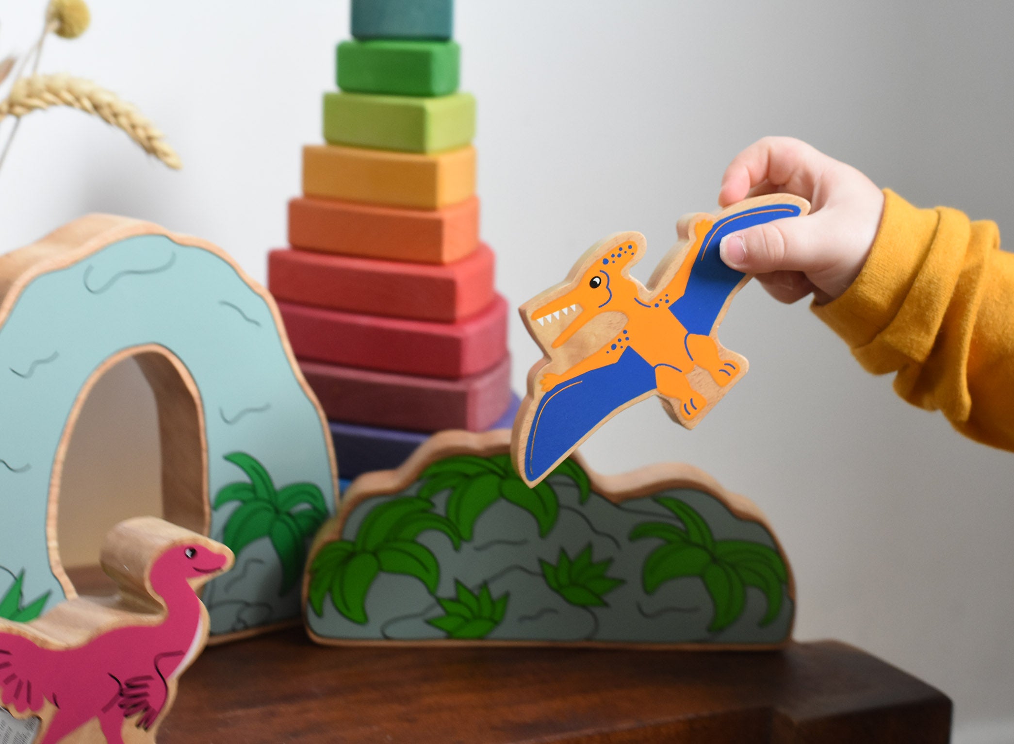 A child playing with Lanka Kade wooden toy dinosaur figures. The child is holding the Lanka Kade pteranodon figure in their hand and flying it through the air. These wooden toy figures are part of a huge range of Lanka Kade fair trade, wooden toys available here at Babipur.
