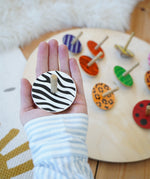 Lanka Kade zebra spinning top in a adult hand above other animal Lanka Kade wooden animal spinning tops on a wooden floor