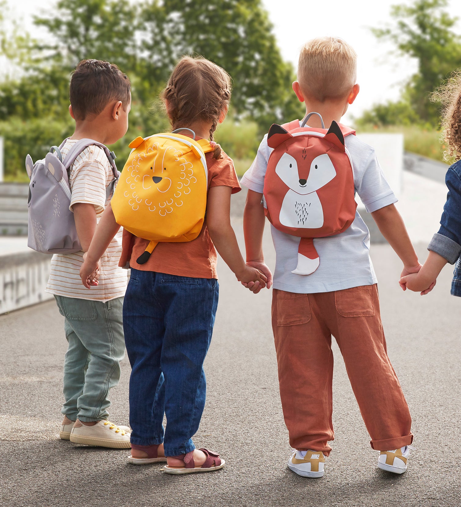 Children holding hands, all wearing Lassig 'About Friends' tiny ids backpacks with different animal styles.