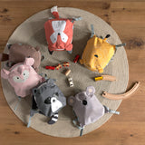 Six Lassig 'About Friends' animal backpacks for kids, laid out on a circular rug with some toys.