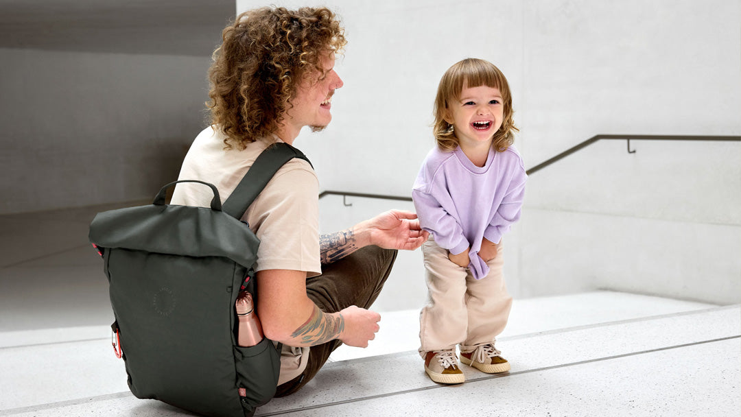 A father wearing a Lassig roll top backpack, laughing with his little daughter.