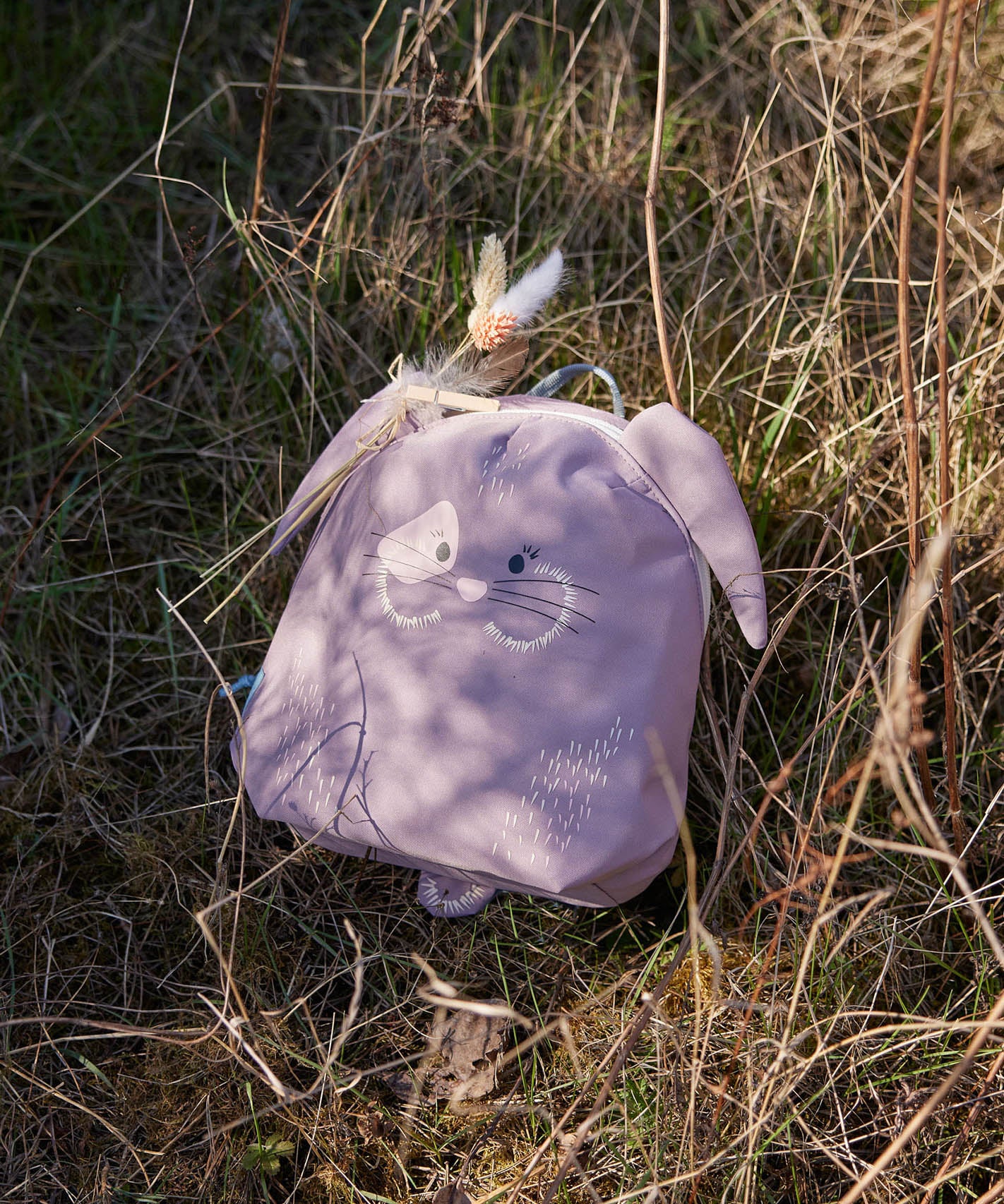 Lassig kids tiny bunny backpack on dry grass with decorative feathers clipped on the backpack with a peg