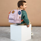 A little boy sat down, wearing the Lassig mini kids backpack in a lilac colour.