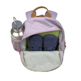 A top view of the Lassig mini kids backpack in a lilac colour, showing how it can fit shoes and books inside, as well as a water bottle in the mesh side pocket.