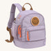 The Lassig mini kids backpack in a lilac colour with orange zips and a smiley face patch.
