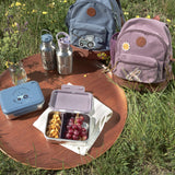 Two Lassig mini kids backpacks, packed ready for a picnic on the grass.