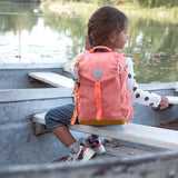 A child on a boat near a river and wearing the Lassig kids mini adventure backpack in rose.