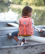 A child on a boat near a river and wearing the Lassig kids mini adventure backpack in rose.