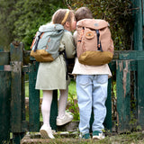 Two kids wearing their Lassig kids mini outdoor backpacks, leaning against a gate.
