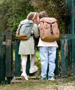 Two kids wearing their Lassig kids mini outdoor backpacks, leaning against a gate.