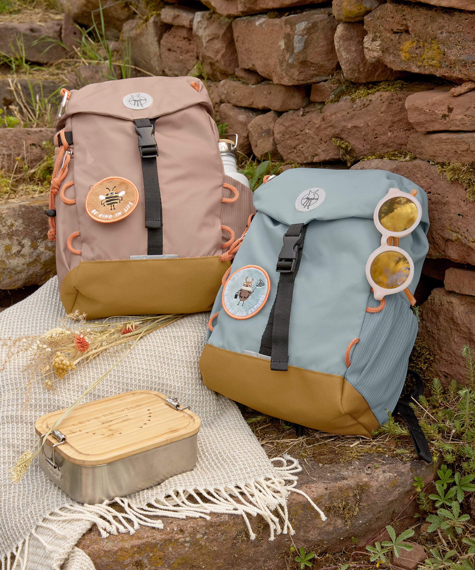 Two Lassig kids mini outdoor backpacks, one in hazelnut brown and another in light blue.