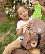 A little girl pulling out the protective waterproof cover from her Lassig mini outdoor backpack in hazelnut.