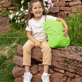 A girl sitting on a wall with her Lassig kids mini outdoor backpack, with the waterproof cover on it.