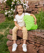 A girl sitting on a wall with her Lassig kids mini outdoor backpack, with the waterproof cover on it.
