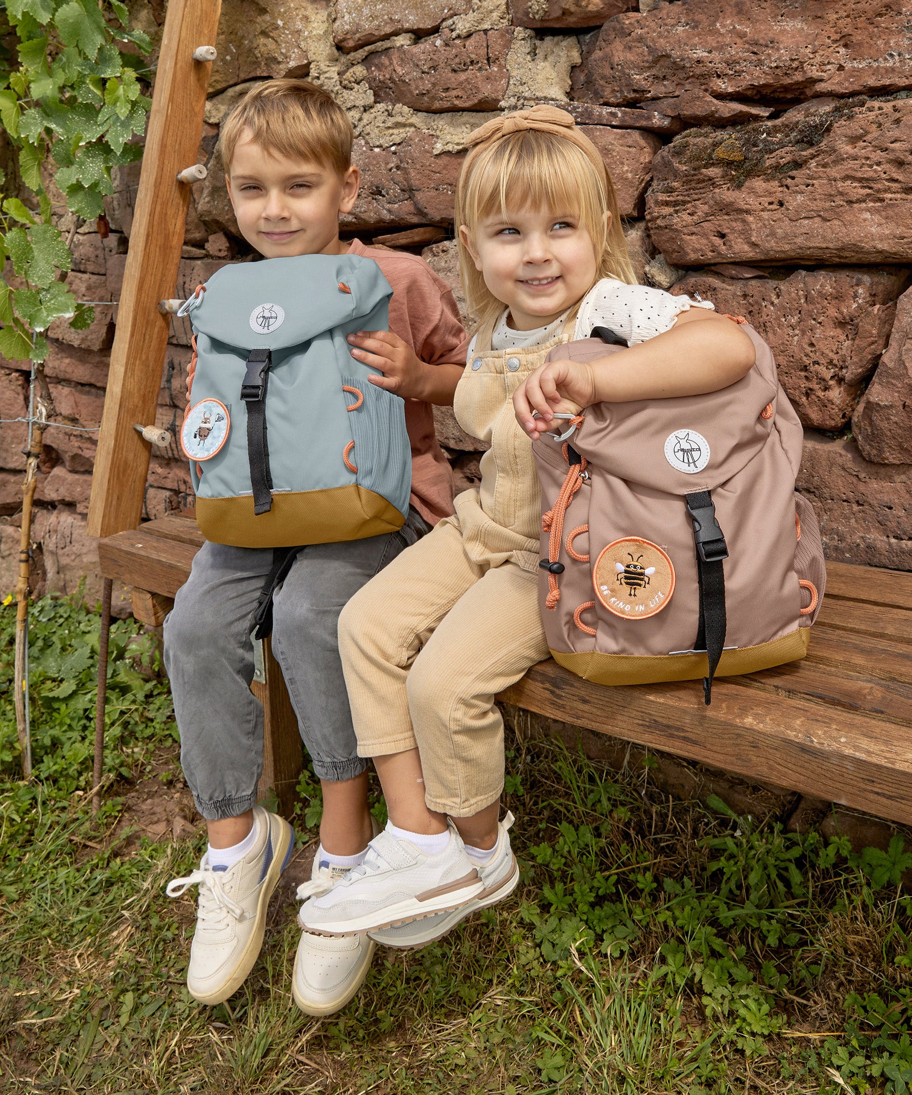 Two children holding their Lassig kids mini outdoor backpack in hazelnut and blue colours.