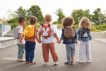 A group of children holding hands, all wearing different 'About Friends' tiny backpacks from Lassig with different animals.