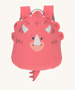 The Lassig tiny kids backpack in a bright coral pink, with a dinosaur face printed on and 3D embellishments and dino tail