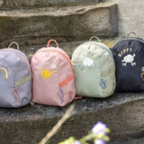 Four Lassig kids tiny backpacks placed on stairs, one is in a light green khaki, one is navy blue, one is pink, and one is pastel purple.