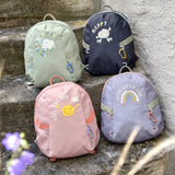 Four Lassig kids tiny backpacks placed on stairs, one is in a light green khaki, one is navy blue, one is pink, and one is pastel purple.