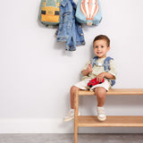 A child sitting on a wooden bench with a digger and balloon character Lassig tiny backpacks hanging from hooks above.