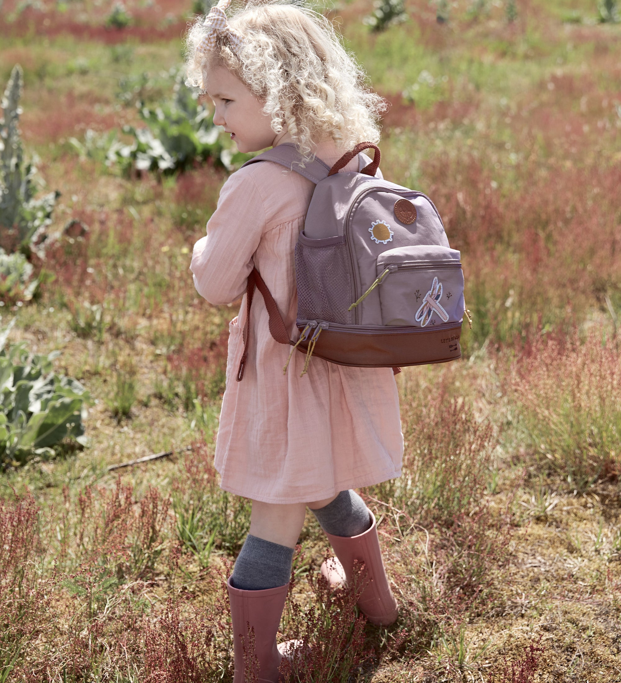 Little girl in a field wearing the Lassig dragonfly mini kids backpack.