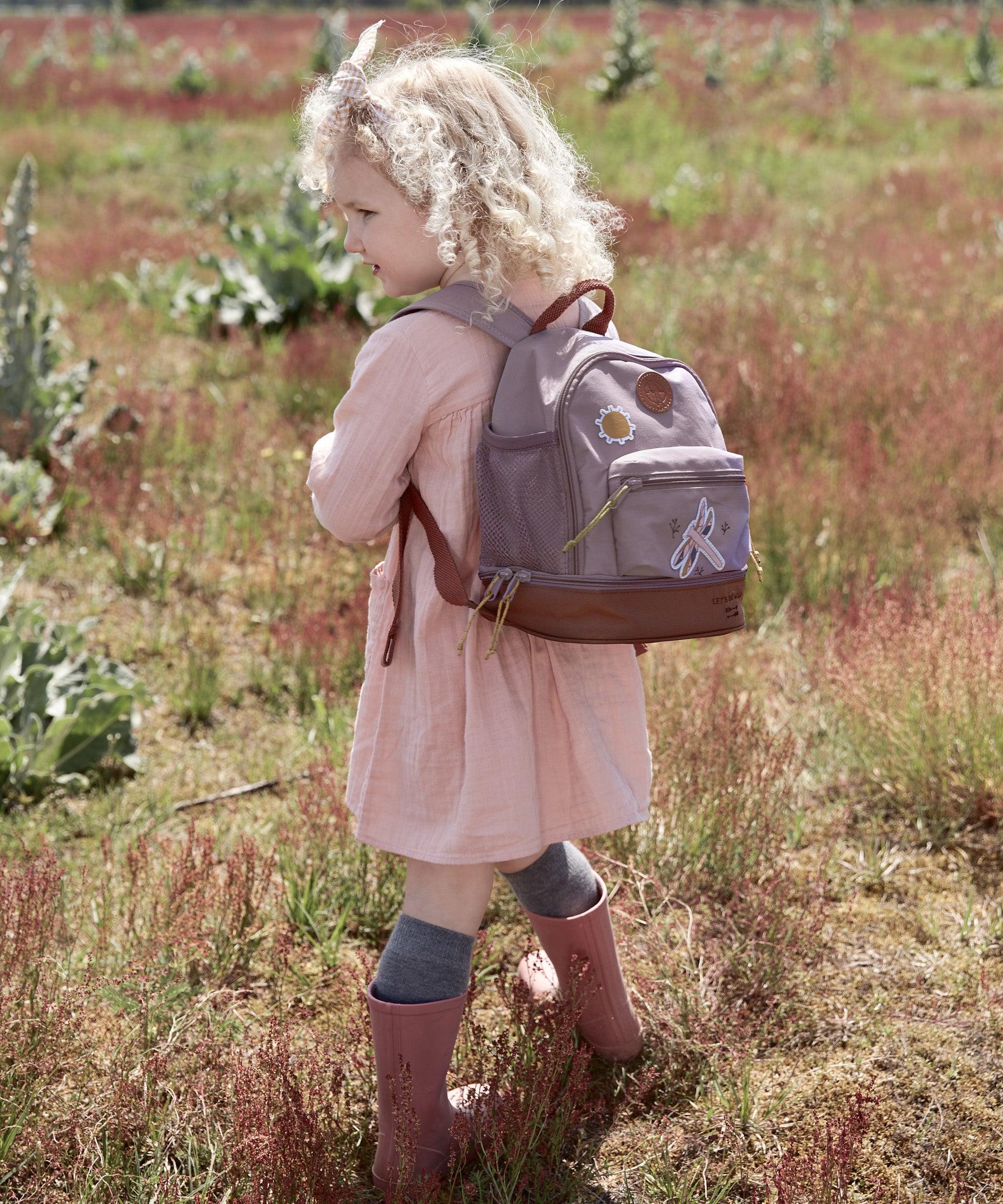 Little girl in a field wearing the Lassig dragonfly mini kids backpack.