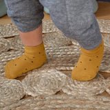 A baby's feet, wearing the Lassig organic cotton baby socks in mustard yellow with navy dots.