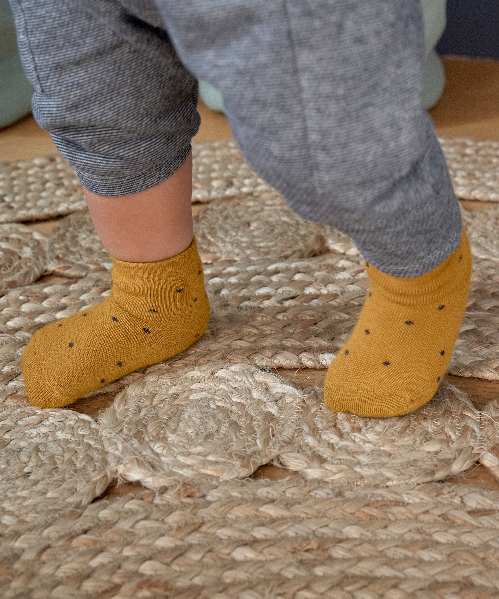 A baby's feet, wearing the Lassig organic cotton baby socks in mustard yellow with navy dots.
