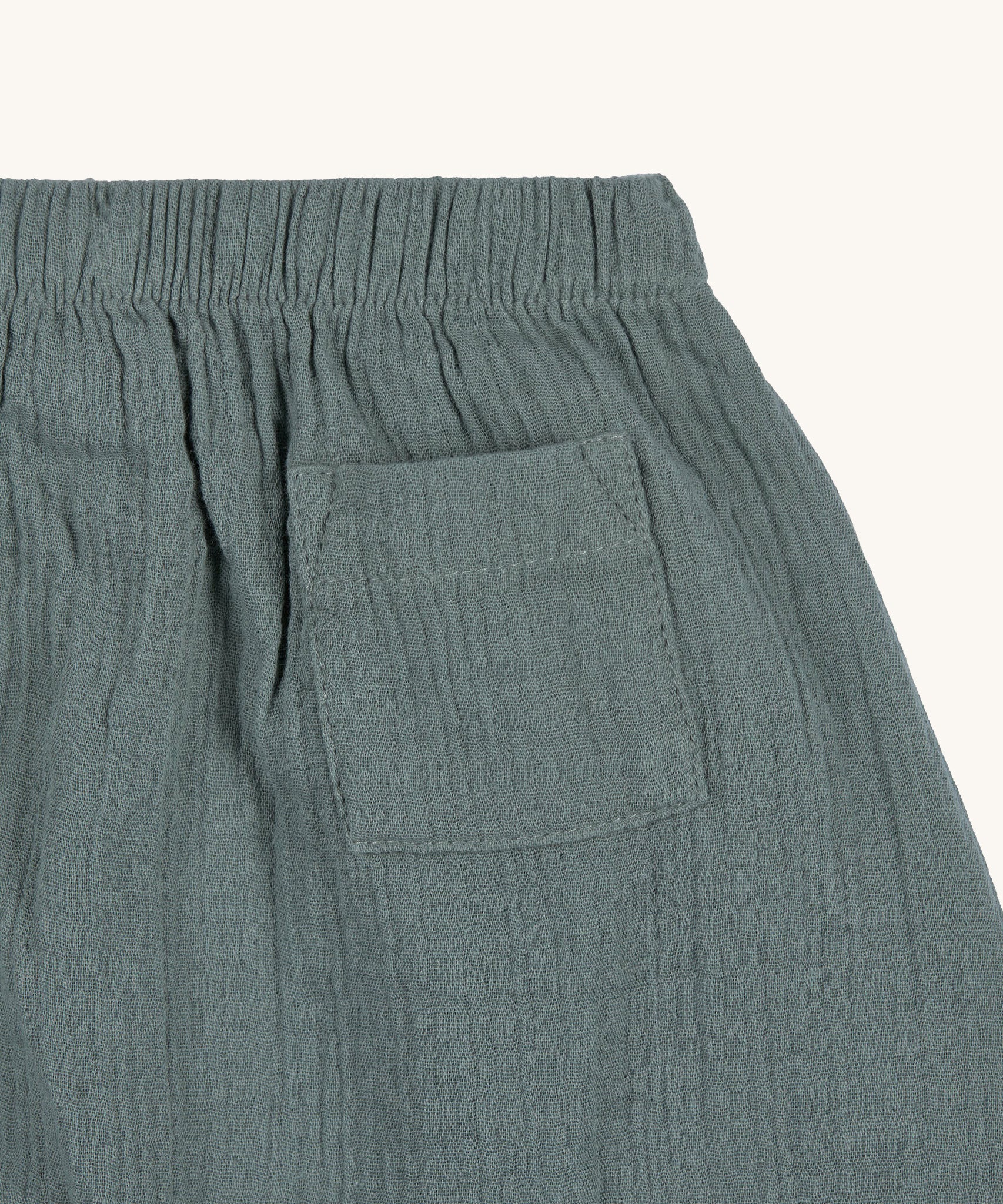 A closeup of the Lassig GOTS organic cotton muslin trousers in petrol green.