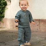 A toddler wearing a Lassig organic cotton muslin outfit in Petrol Green.