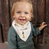 A smiling baby in a Lassig organic cotton muslin outfit in petrol green, and a Lassig dribble bib.