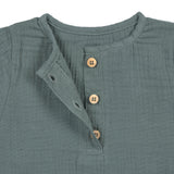 A closeup of the brown buttons on the Lassig organic cotton muslin long sleeved top for babies and toddlers, in a dark petrol green.