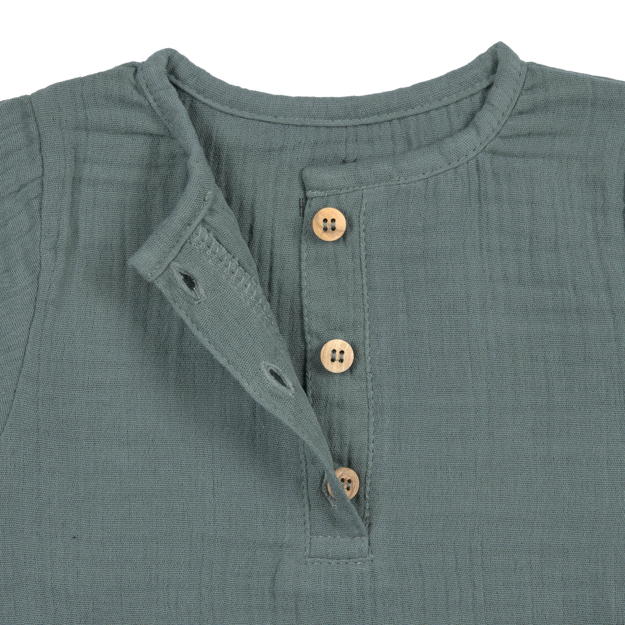 A closeup of the brown buttons on the Lassig organic cotton muslin long sleeved top for babies and toddlers, in a dark petrol green.